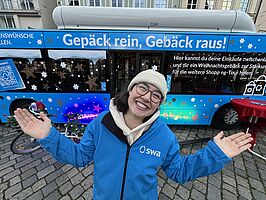 Frau steht lachend mit swa Jacke vor einem Bus mit swa Gepäck rein, Gebäck raus Branding