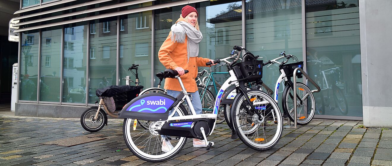 Frau mit mechanischen Fahrrad swabi steht neben Fahrradständern mit abgestellten Fahrrädern