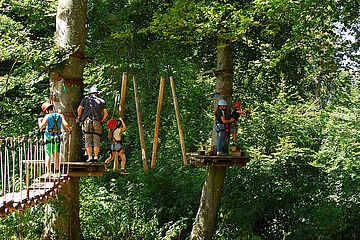 Menschen mit Schutzkleidung und -gurten auf Anlagen des Augsburger Kletterwalds. Ein Klick sorgt für eine Großansicht des Bildes.