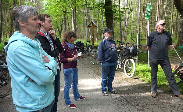 Personen stehen nebeneinander auf einem Waldweg. Im Hintergrund stehen ihre Fahrräder.