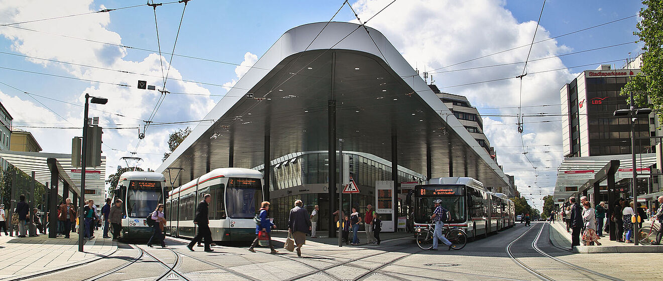 Frontansicht der Haltestelle "Königsplatz" mit Menschen Bussen und Straßenbahnen