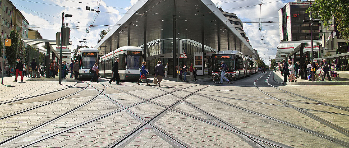 Frontansicht der Haltestelle "Königsplatz" mit Menschen Bussen und Straßenbahnen