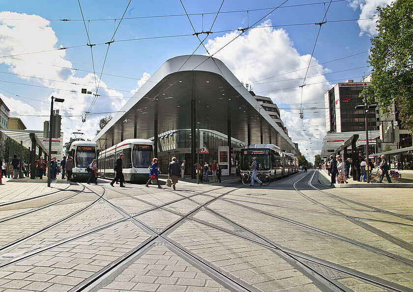 Frontansicht der Haltestelle "Königsplatz" mit Menschen Bussen und Straßenbahnen