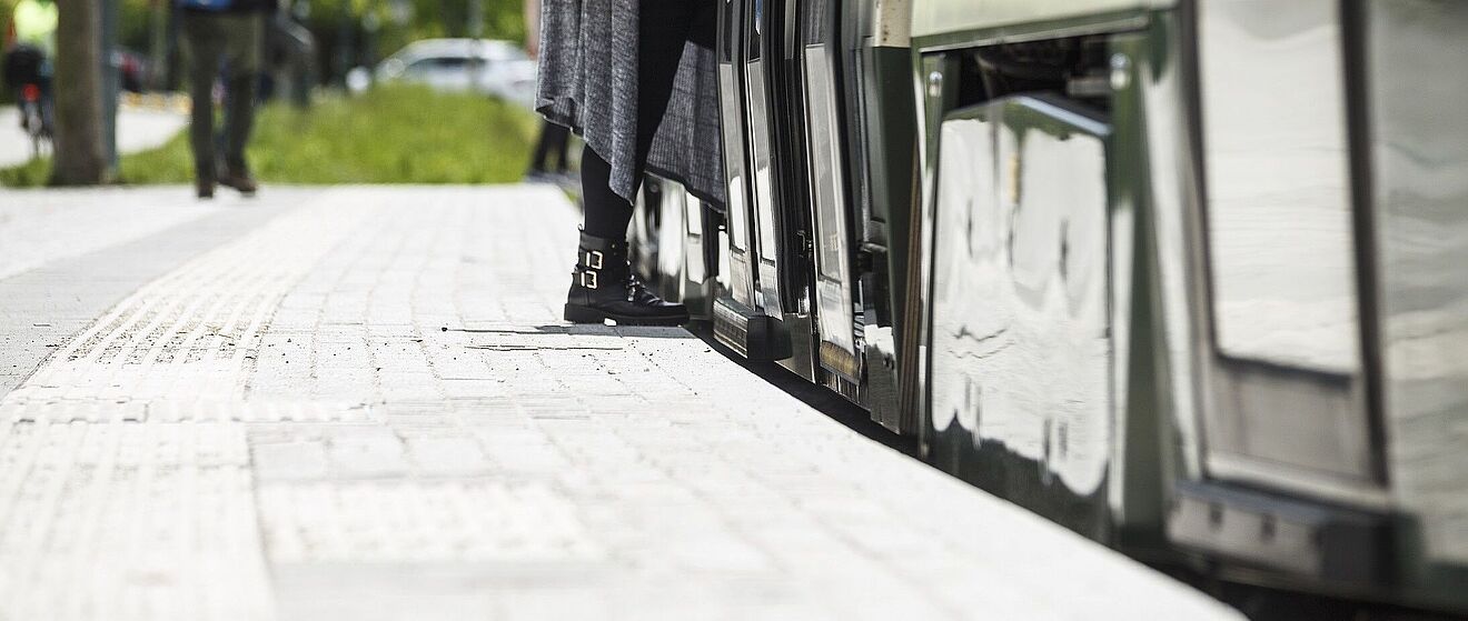 Eine Person steigt in eine Straßenbahn der swa ein. auf dem Boden sind Streifen für Barrierefreiheit zu erkennen.