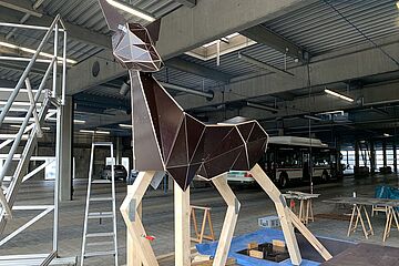 Rahmen einer Rehskulptur in einer Lagerhalle. Im Hintergrund ist ein Bus. Ein Klick sorgt für eine Großansicht des Bildes.