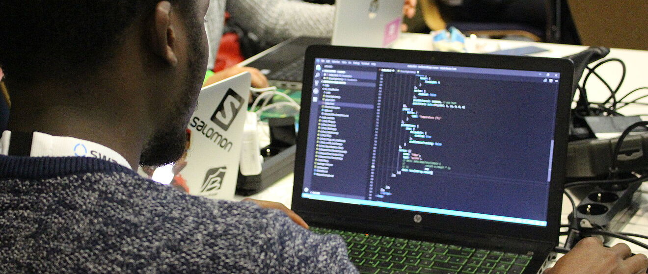 Ein Mann sitzt vor einem Laptop und führt Programmierungen durch.