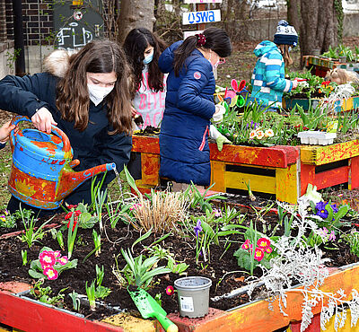 Kinder gießen mit einer Gießkanne draußen Blumenbeete.