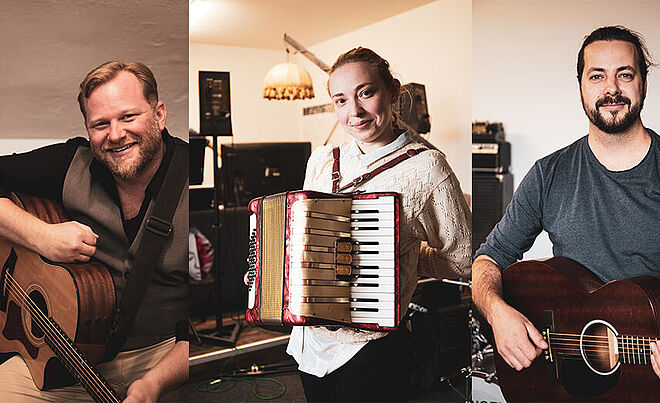 Drei Musiker mit ihren Instrumenten. Zwei Männer mit Gitarre und eine Frau mit Ziehharmonika.