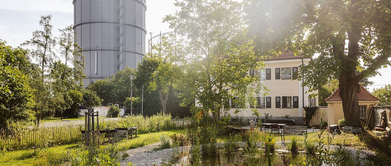 Gaskessel im Gaswerk. Im Vordergrund sind Bäume und ein Gebäude.