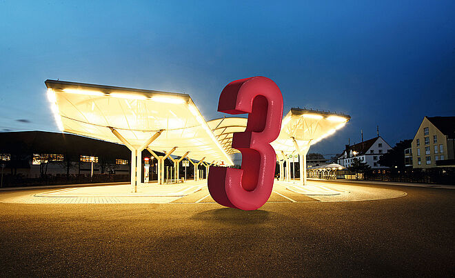 Eine große 3 vor einer Haltestelle.