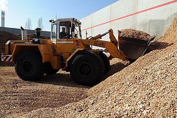 Ein Baustellenfahrzeug transportiert Sägespäne im Biomasse Heizkraftwerk. - Ein Klick auf das Bild führt zur vergrößerten Fotoansicht.