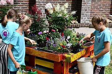 Mädchen füllen erde in ihr selbst gebautes Hochbeet. Ein Klick auf das Bild ermöglicht eine größere Anzeige.