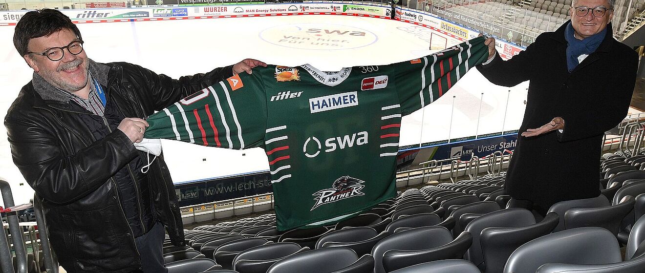 Zwei Männer präsentieren neues AEV-Trikot im AEV Stadion
