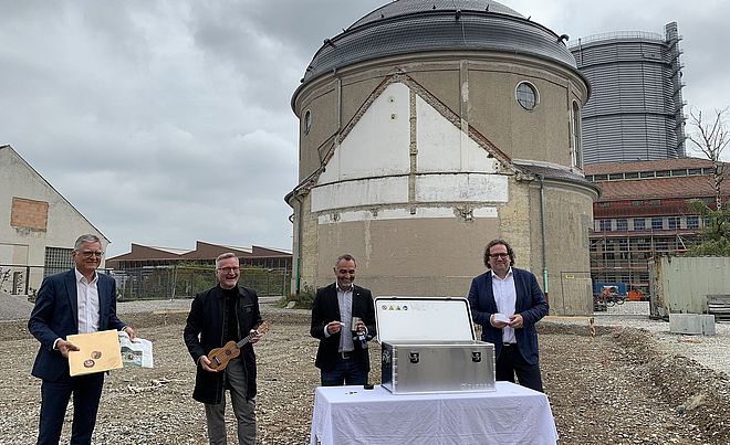 Vier Männer stehen mit Zeitungen und Instrumenten vor einem Tisch auf dem eine Box steht. Weiterverlinkung auf Musikbox Newsartikel