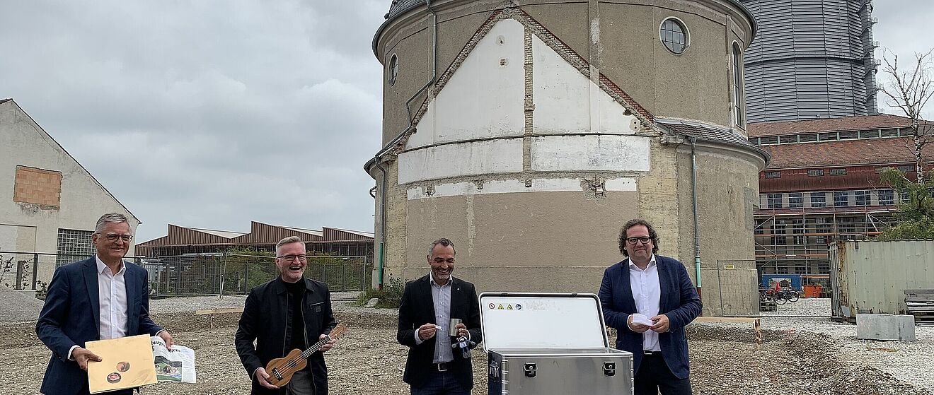 Vier Männer stehen mit Zeitungen und Instrumenten vor einem Tisch auf dem eine Box steht. Weiterverlinkung auf Musikbox Newsartikel