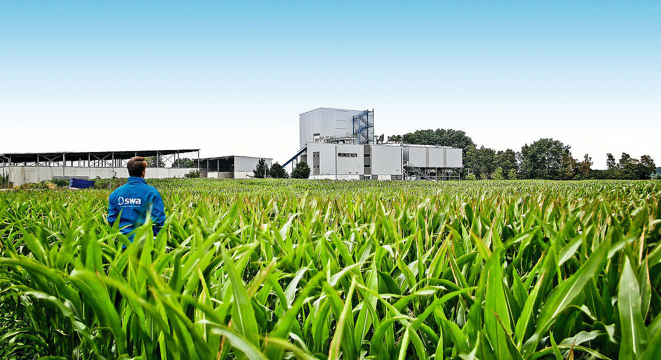 Mann mit blauer swa Jacke auf einem Feld. Im Hintergrund ist ein swa Kraftwerk zu sehen