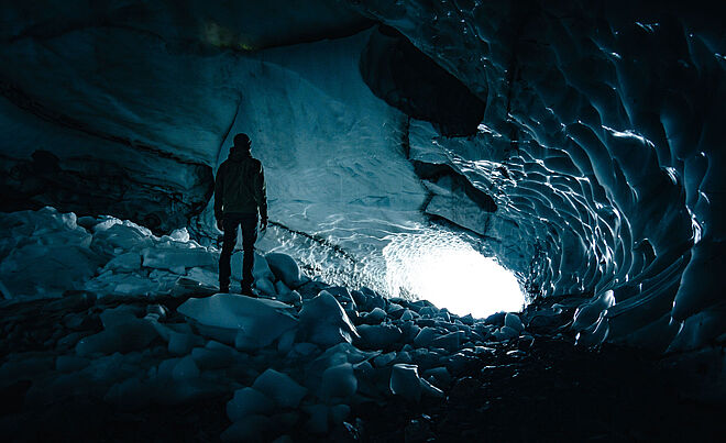 Bodenansicht von einer Gletscherhöhle, in der Christian zum Ausgang gerichtet steht.