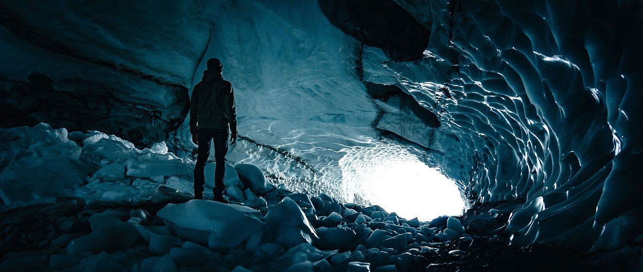 Bodenansicht von einer Gletscherhöhle, in der Christian zum Ausgang gerichtet steht.