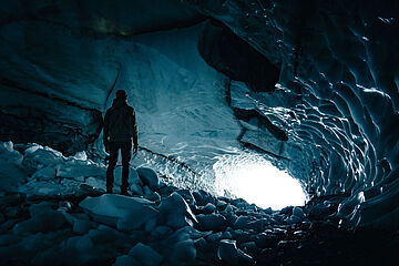Bodenansicht von einer Gletscherhöhle, in der Christian zum Ausgang gerichtet steht.