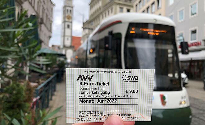 Foto eines AVV/swa 9-Euro-Tickets, im Hintergrund ist eine swa Tram zu sehen.