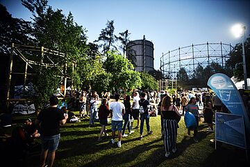 Menschenmenge läuft auf dem Gaswerksgelände. Im Hintergrund ist der Gaskessel. - Ein Klick auf das Bild führt zur vergrößerten Fotoansicht.
