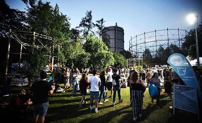 Menschenmenge läuft auf dem Gaswerksgelände. Im Hintergrund ist der Gaskessel. Weiterverlinkung auf Modular Anreise Newsartikel