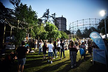 Menschenmenge läuft auf dem Gaswerksgelände. Im Hintergrund ist der Gaskessel. Ein Klick auf das Bild führt zu einer größeren Ansicht.