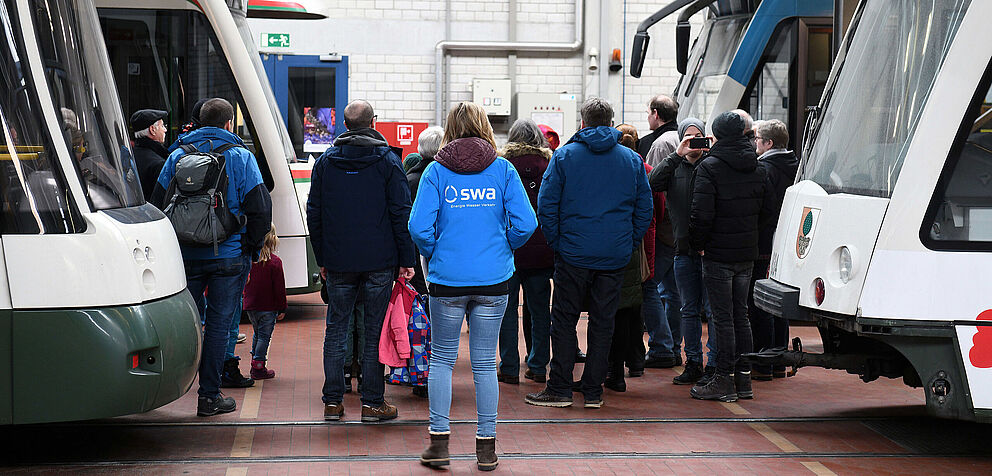 Führung mit Gästen und Mitarbeitern in swa Jacke im Straßenbahnbetriebshof. Links und rechts sind Straßenbahnen