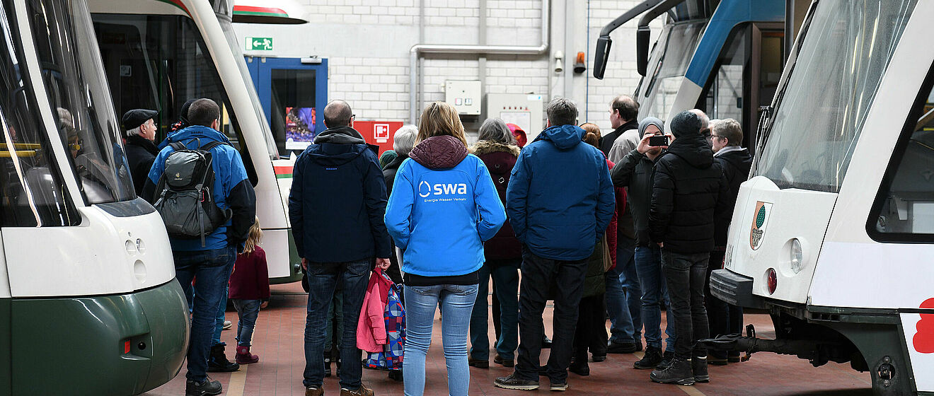 Führung mit Gästen und Mitarbeitern in swa Jacke im Straßenbahnbetriebshof. Links und rechts sind Straßenbahnen