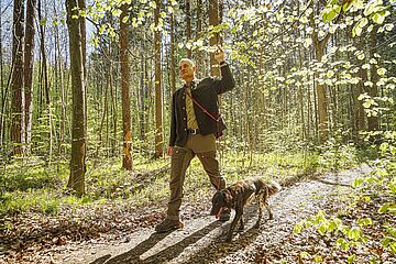Förster läuft mit seinem Hund durch einen Wald und betrachtet die Bäume. - Ein Klick auf das Bild führt zur vergrößerten Fotoansicht.
