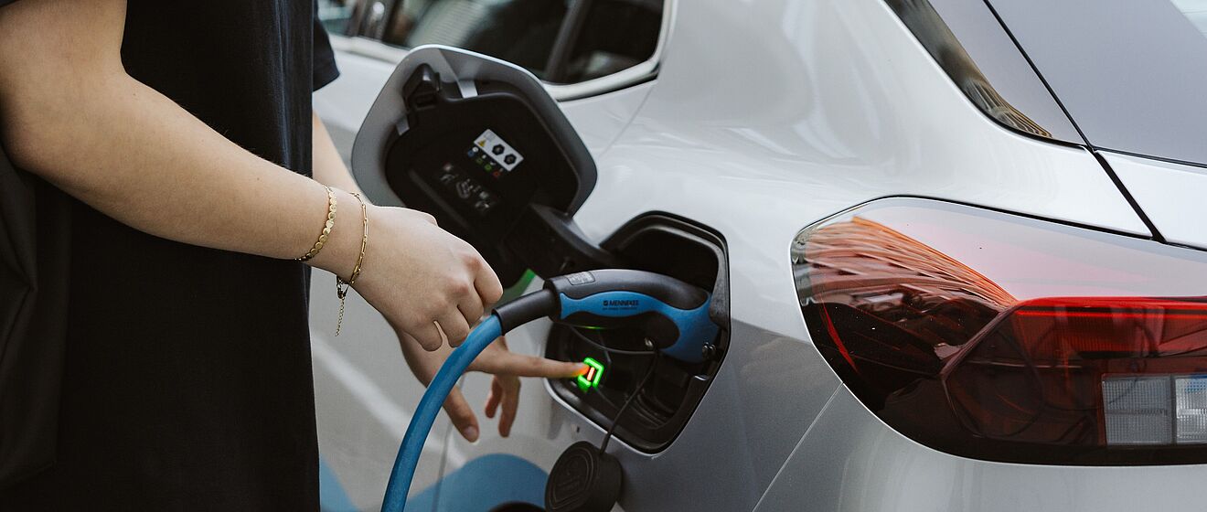 Person mit Schmuck am Arm schließt Carsharing Auto an E-Ladesäule an und betätigt einen Knopf am Tankdeckel