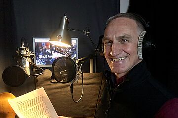 Mann mit Kopfhörern mit einem Skript in der Hand steht vor einem Mikrofon