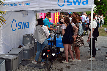 Personen im blauen Tshirt schenken Leute Wasser aus dem swa Wasserlastenrad aus