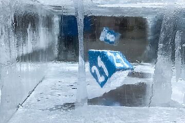 Ein großer, beleuchteter Eisblock, in den mehrere kleinere, blaue Würfel eingefroren sind, die Zahlen zeigen, darunter die Zahl 