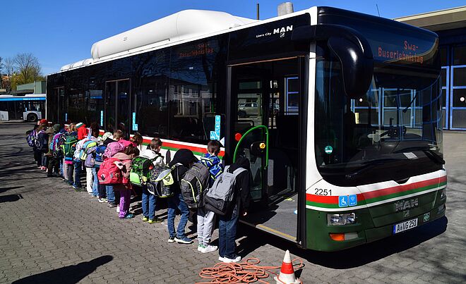 Schulkinder mit Rucksack beim Bussicherheitstraining. Die Kinder sind zu einem swa Bus im Hintergrund gedreht