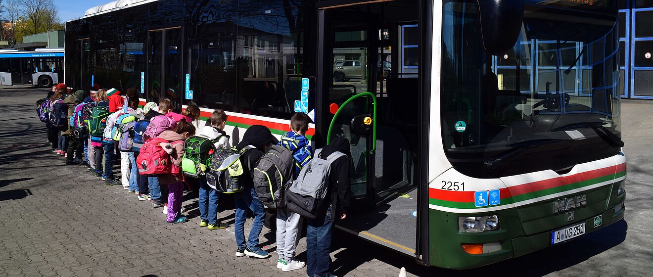 Schulkinder mit Rucksack beim Bussicherheitstraining. Die Kinder sind zu einem swa Bus im Hintergrund gedreht