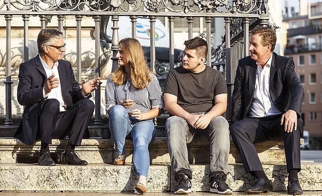 Vier Personen sitzen vor dem Augustusbrunnen und führen angeregte Gespräche.