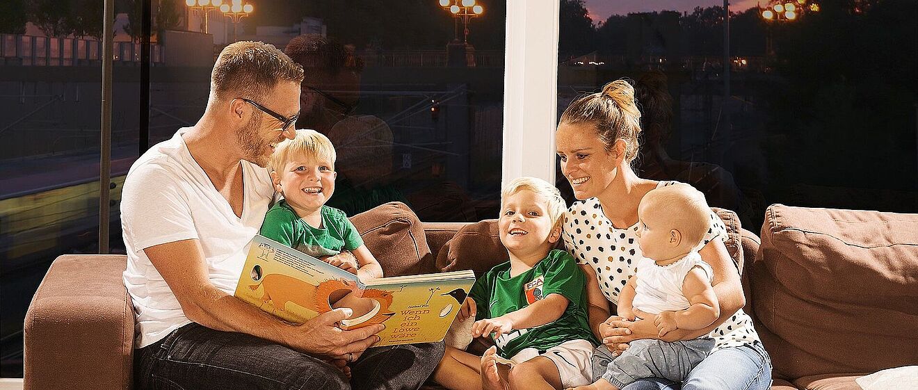 Familie, die gemütlich zusammen auf der Couch sitzt und ein Kinderbuch liest. 