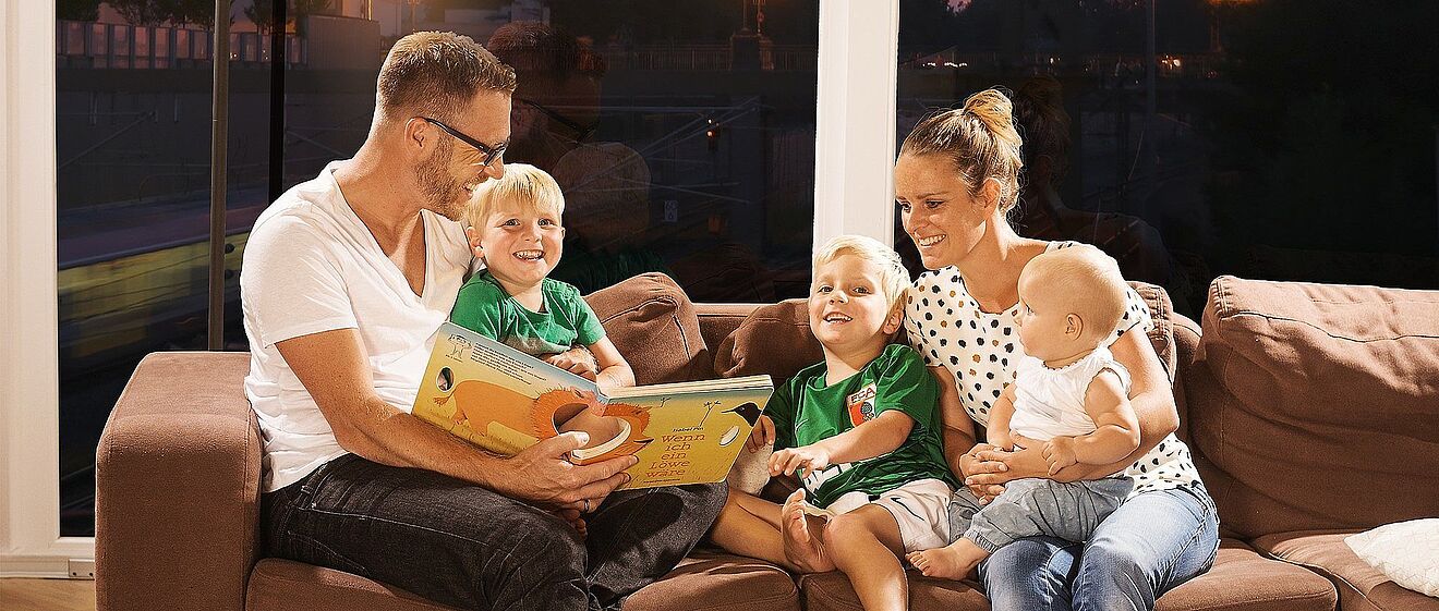 Familie, die gemütlich zusammen auf der Couch sitzt und ein Kinderbuch liest. 