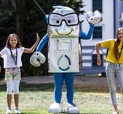 Zwei Mädchen stehen mit Oswald auf einer Wiese und lachen.