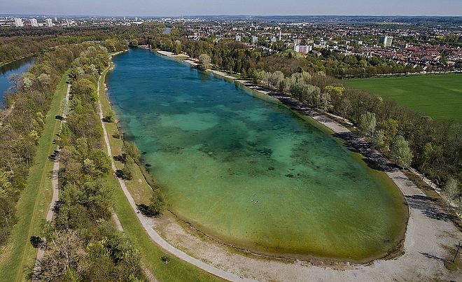 Ein großer See befindet sich inmitten einer Naturlandschaft mit Bäumen und Gehwegen.