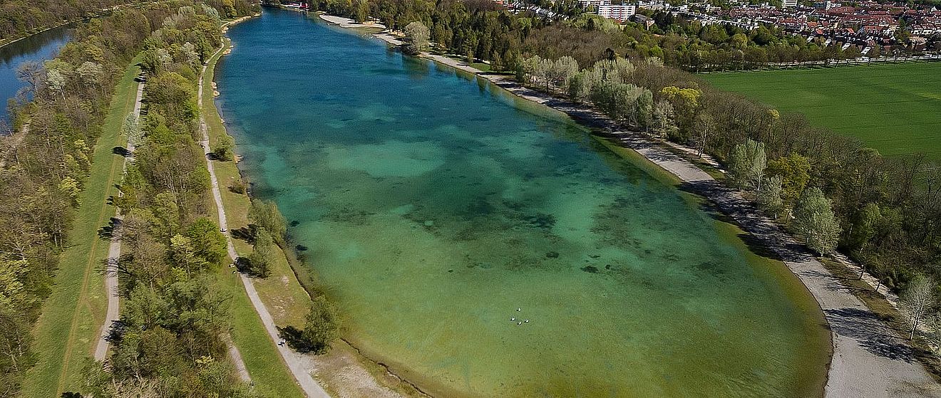 Ein großer See befindet sich inmitten einer Naturlandschaft mit Bäumen und Gehwegen.