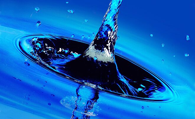 Nahaufnahme eines Wassertropfens, der in eine Wasseroberfläche fällt und eine Spritzsäule erzeugt.