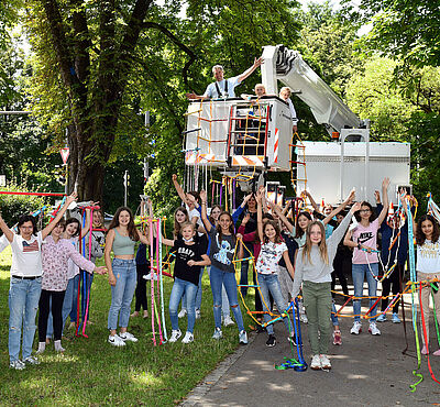 Kinder mit Himmelsleitern in den Händen, im Hintergrund eine weiße Hebebühne.