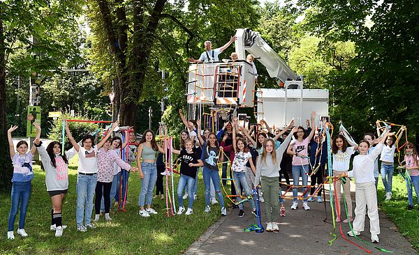 Kinder mit Himmelsleitern in den Händen, im Hintergrund eine weiße Hebebühne.
