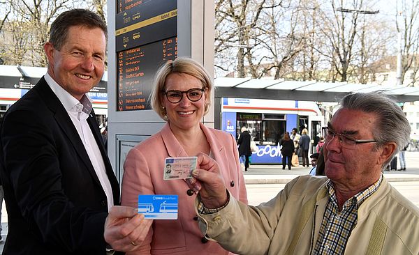 Drei Männer und eine Frau stehen lächelnd am Augsburger Königsplatz. Der Mann auf der linken Seite hält eine swa Fahrkarte in der Hand, der andere seinen Führerschein. 