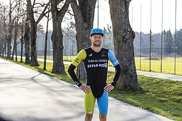 Triathlet Lukas Stahl posiert mit swa Kappe auf einem Weg vor Bäumen