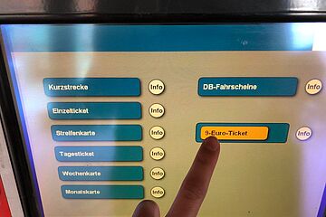 Foto eines Fingers, der auf die 9-Euro-Ticket Taste auf dem Screen eines Fahrkartenautomaten drückt. - Ein Klick auf das Bild führt zur vergrößerten Fotoansicht.