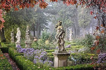 Steinstatuen in einem Garten mit Bäumen und Blumen in der Stadt Rothenburg ob der Tauber. Ein Klick sorgt für eine Großansicht des Bildes