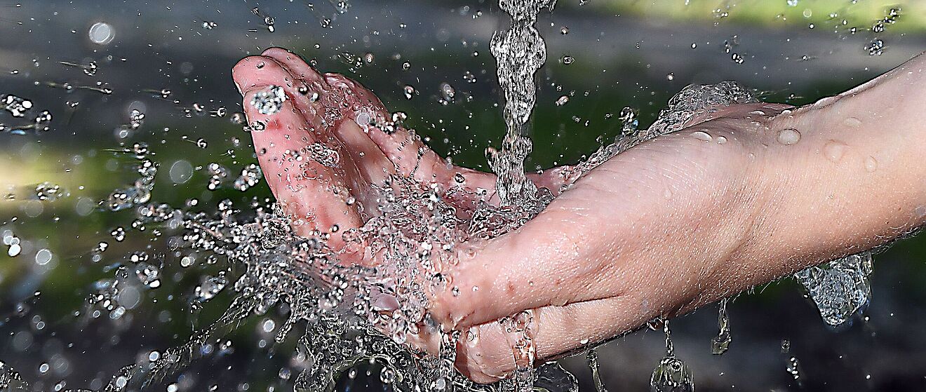Hand unter einem Wasserstrahl. Link zum Öffnen eines Pop-Ups mit Informationen zur wirtschaftlichen Wasserversorgung